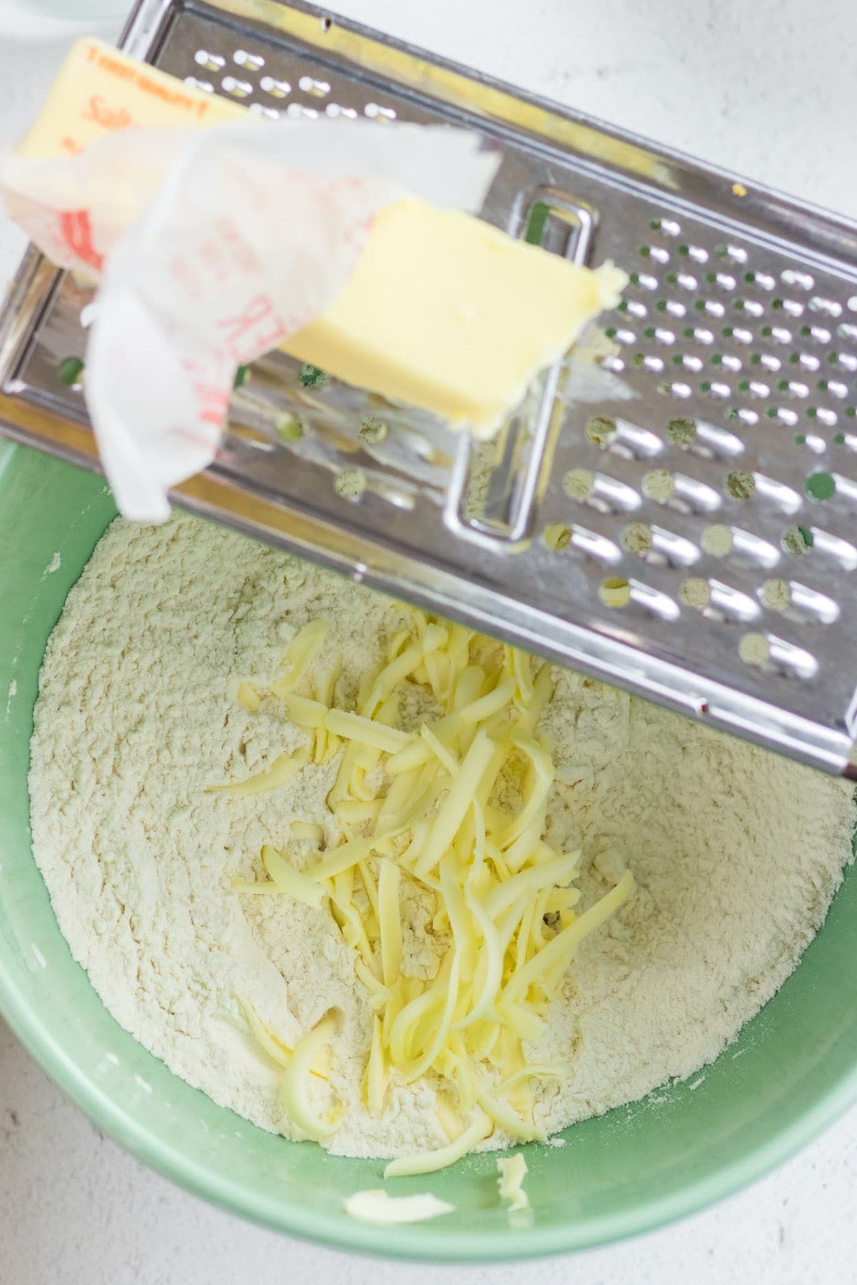 Cold butter being grated into a bowl of flour.