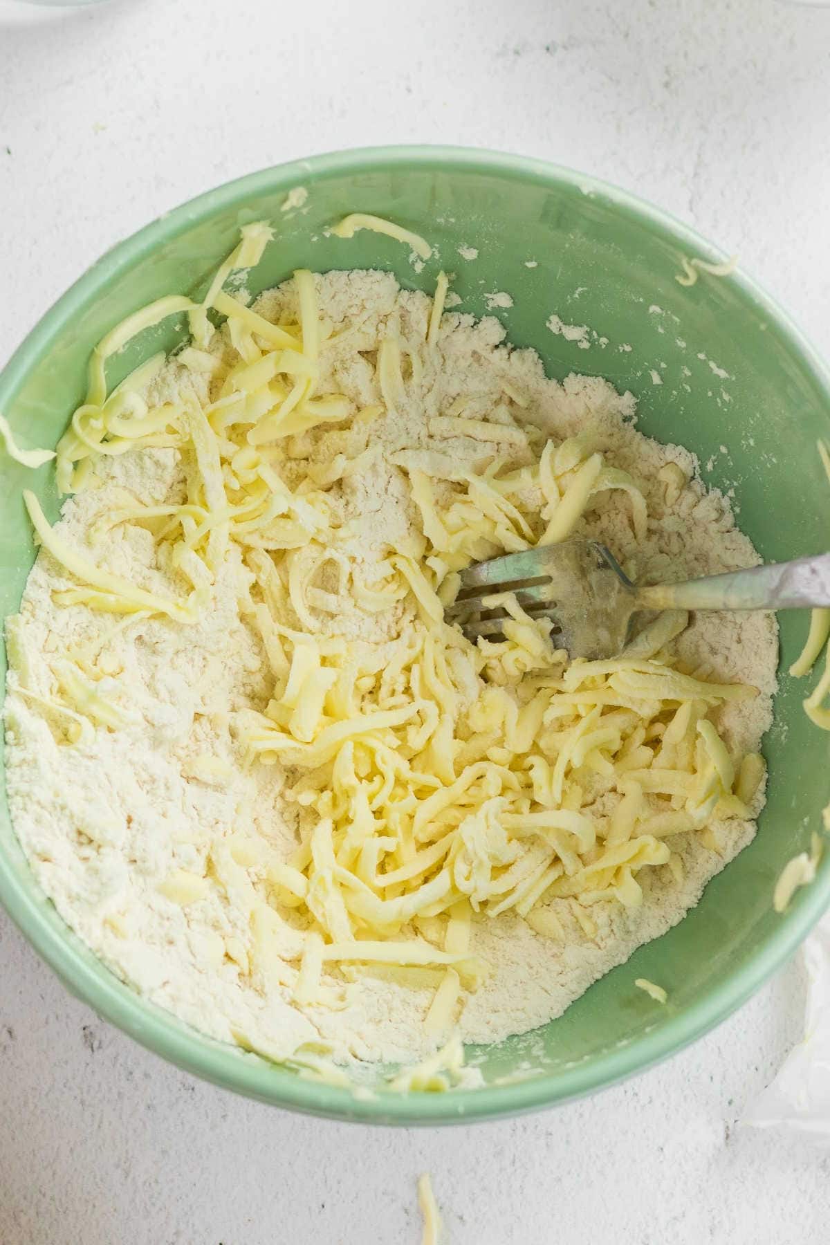 Grated butter being mixed into the flour with a fork.
