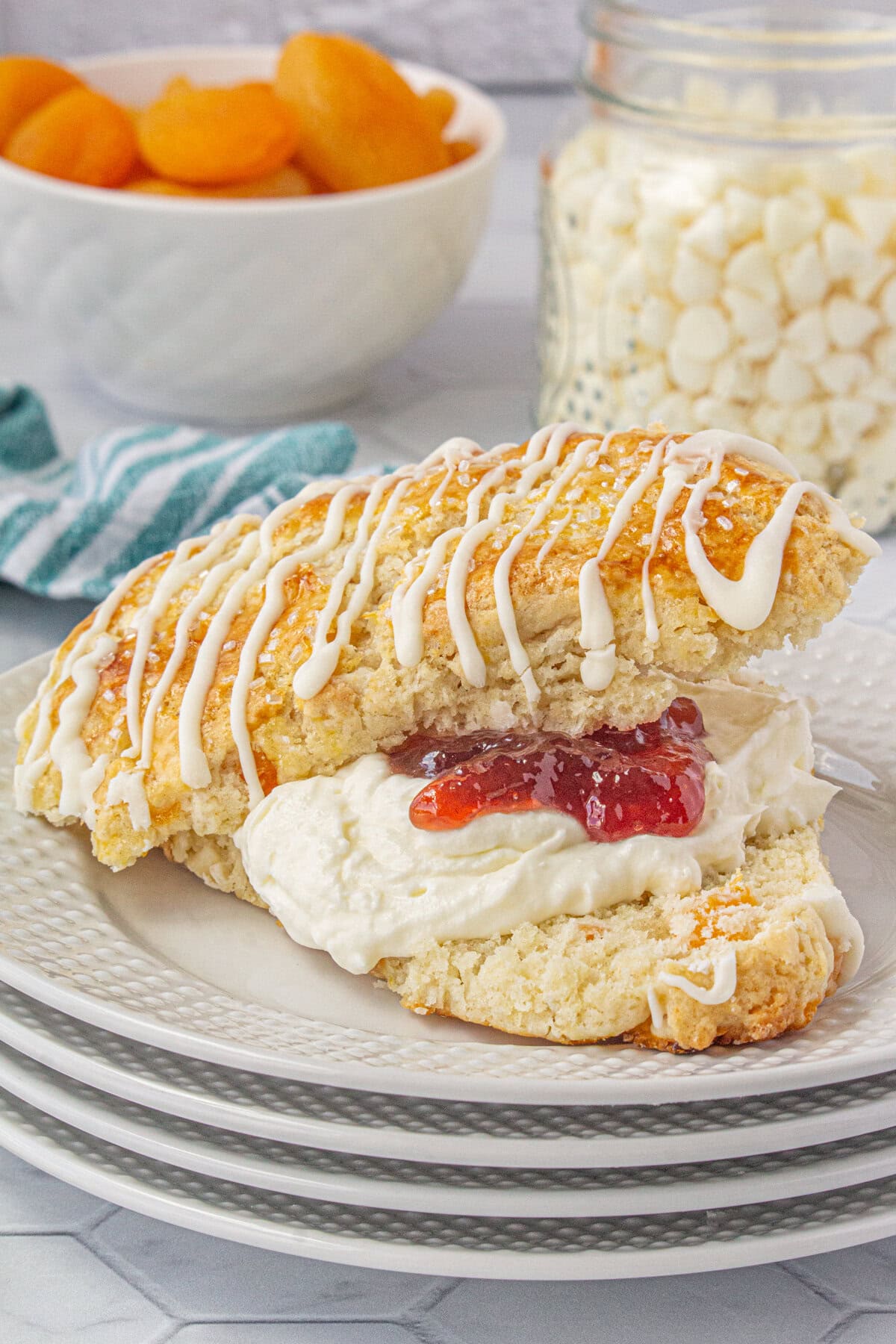 An apricot white chocolate scone split in half and filled with cream and jam.