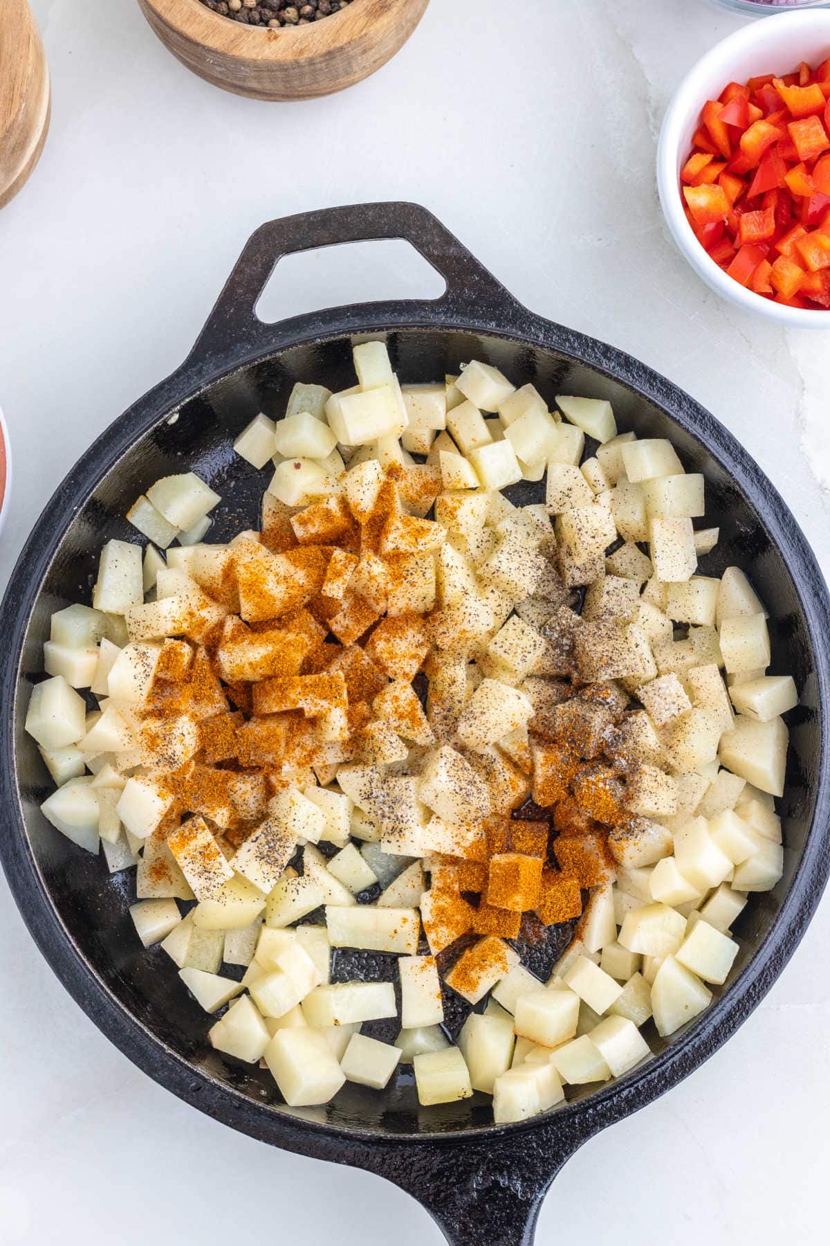 Diced potatoes in an iron skillet with chili powder and seasoning sprinkled on top.