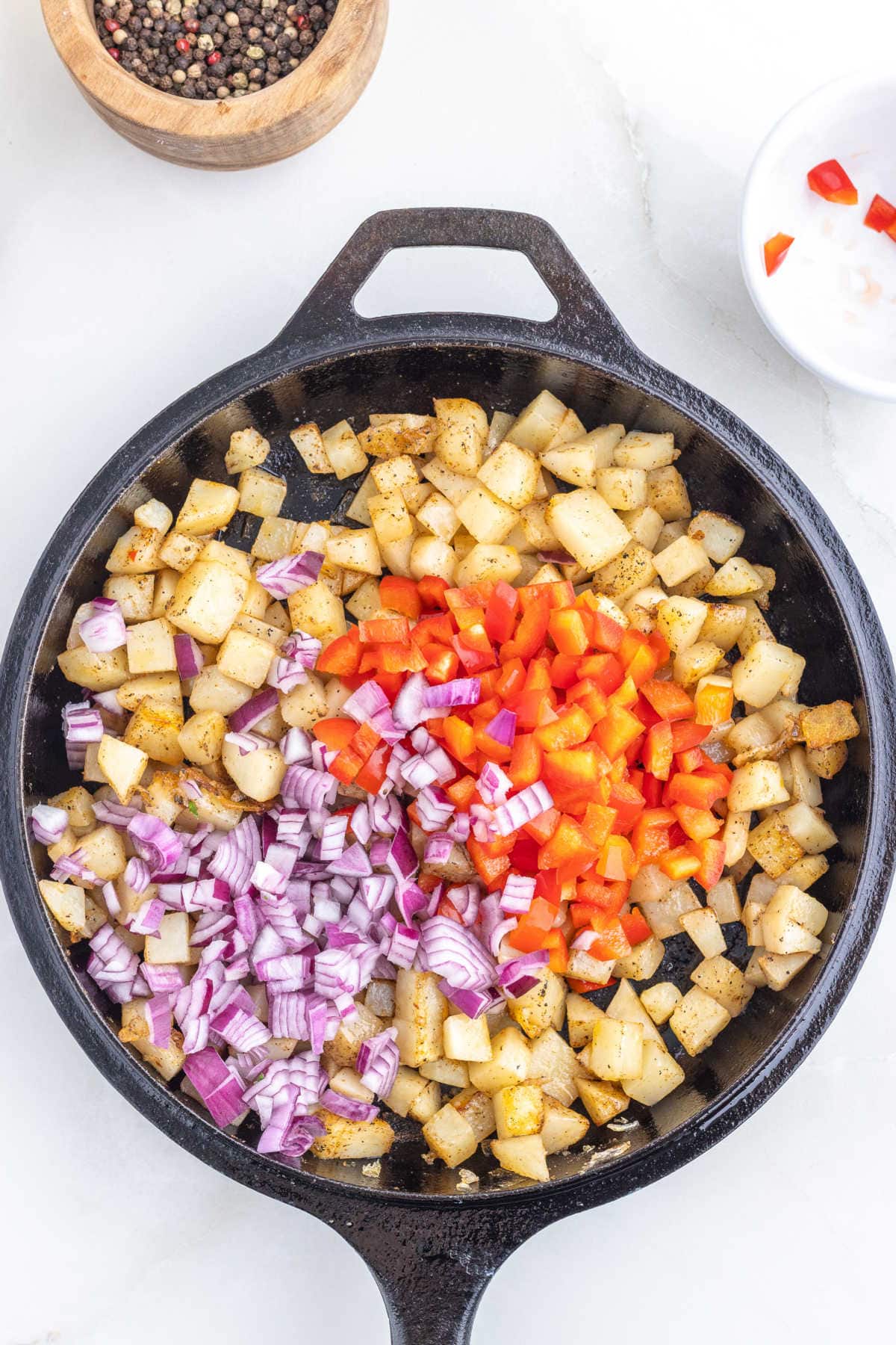 Partially cooked potatoes in a skillet with onions and bell peppers added.