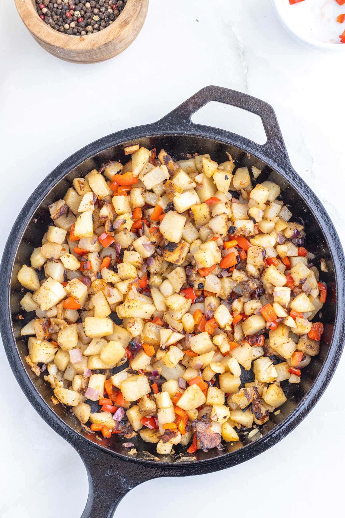 Potatoes, onions, and peppers in the iron skillet are cooked and ready to eat.