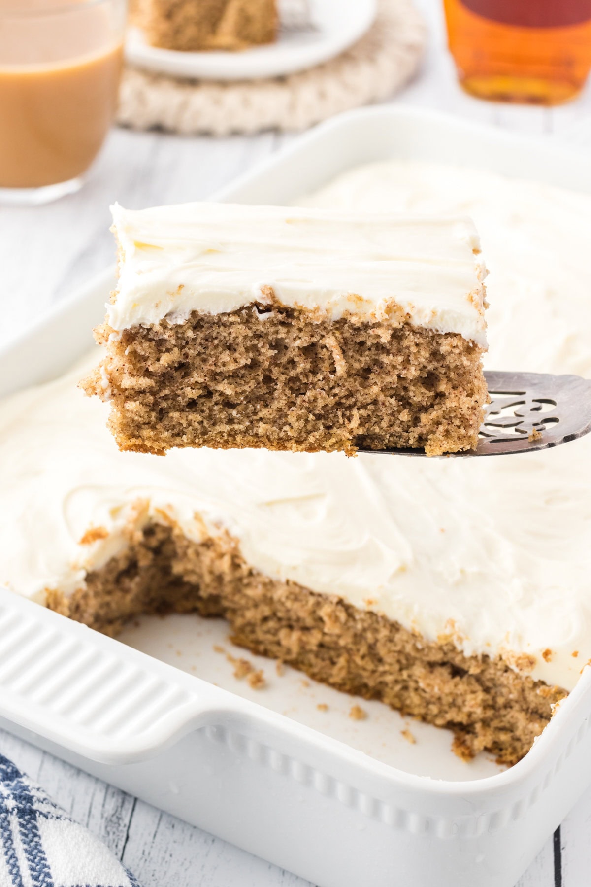 A slice of golden brown spice cake with a creamy frosting being removed from the cake pan.