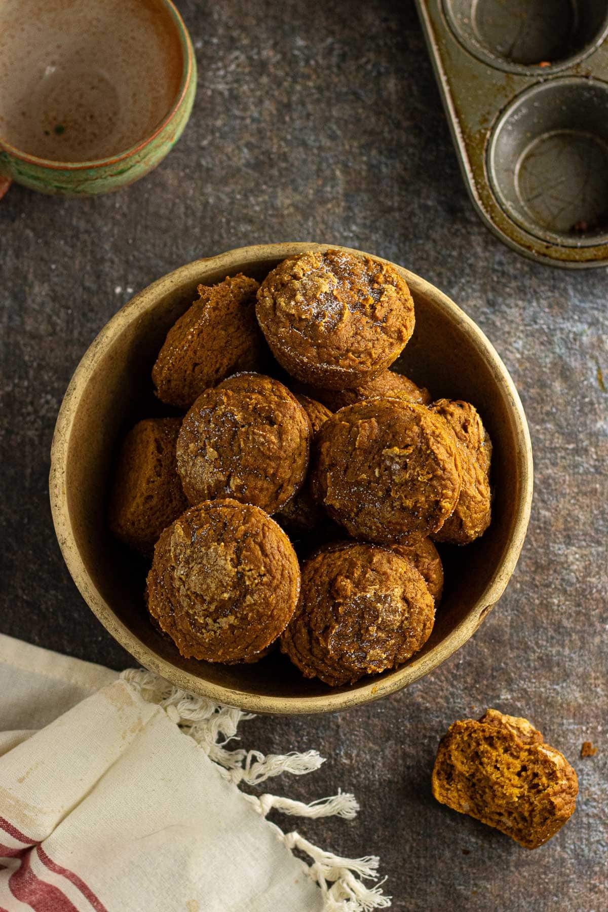 An overhead view of the pumpkin muffins in a bowl. One off to the side has a few bites taken out.