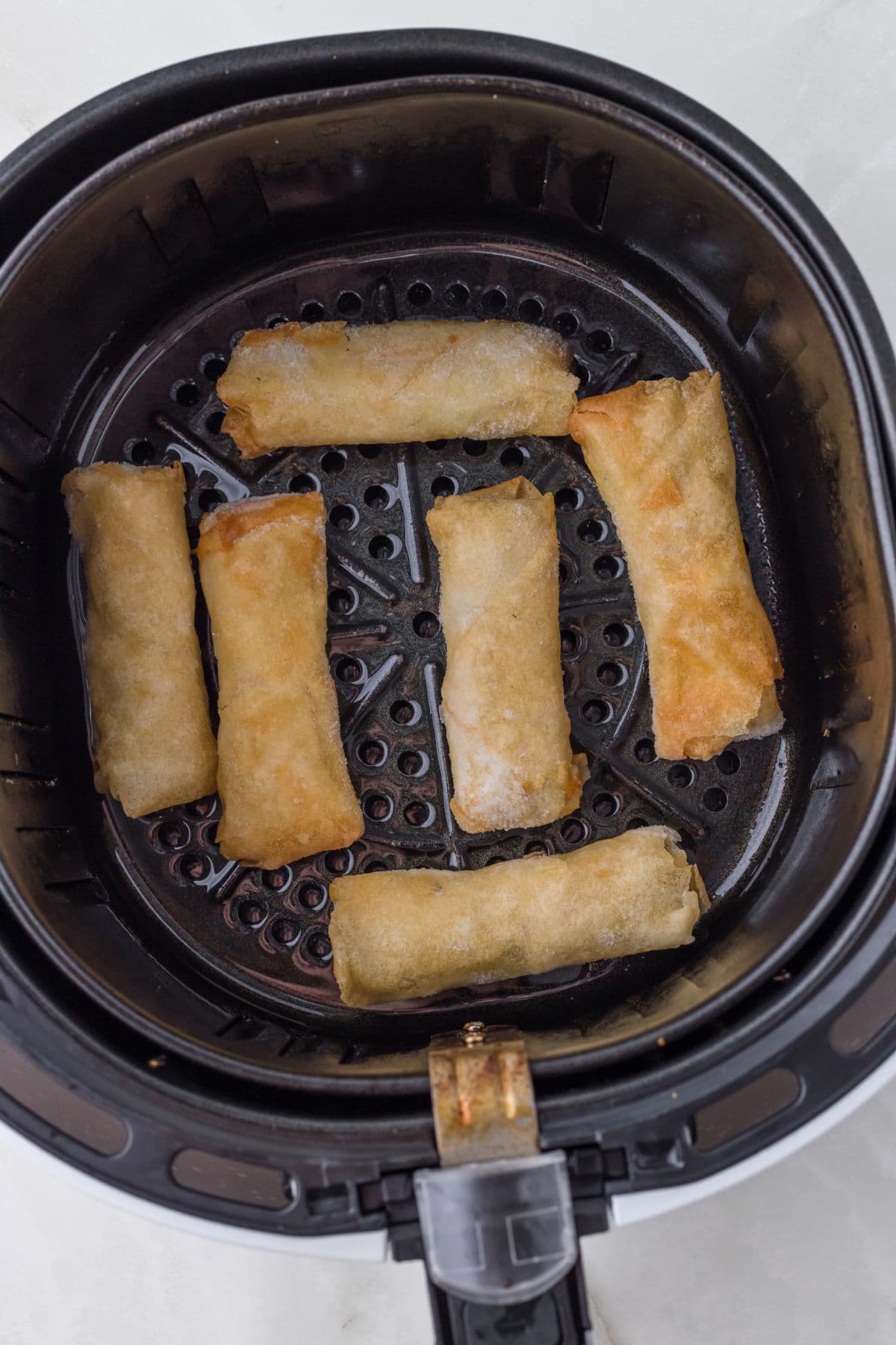 Finished spring rolls in an air fryer basket.