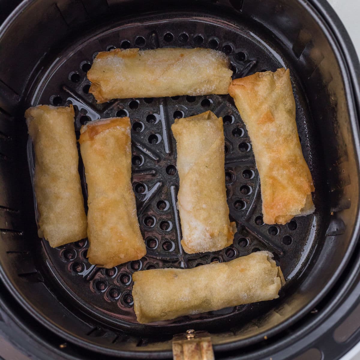 Golden brown spring rolls in an air fryer basket.