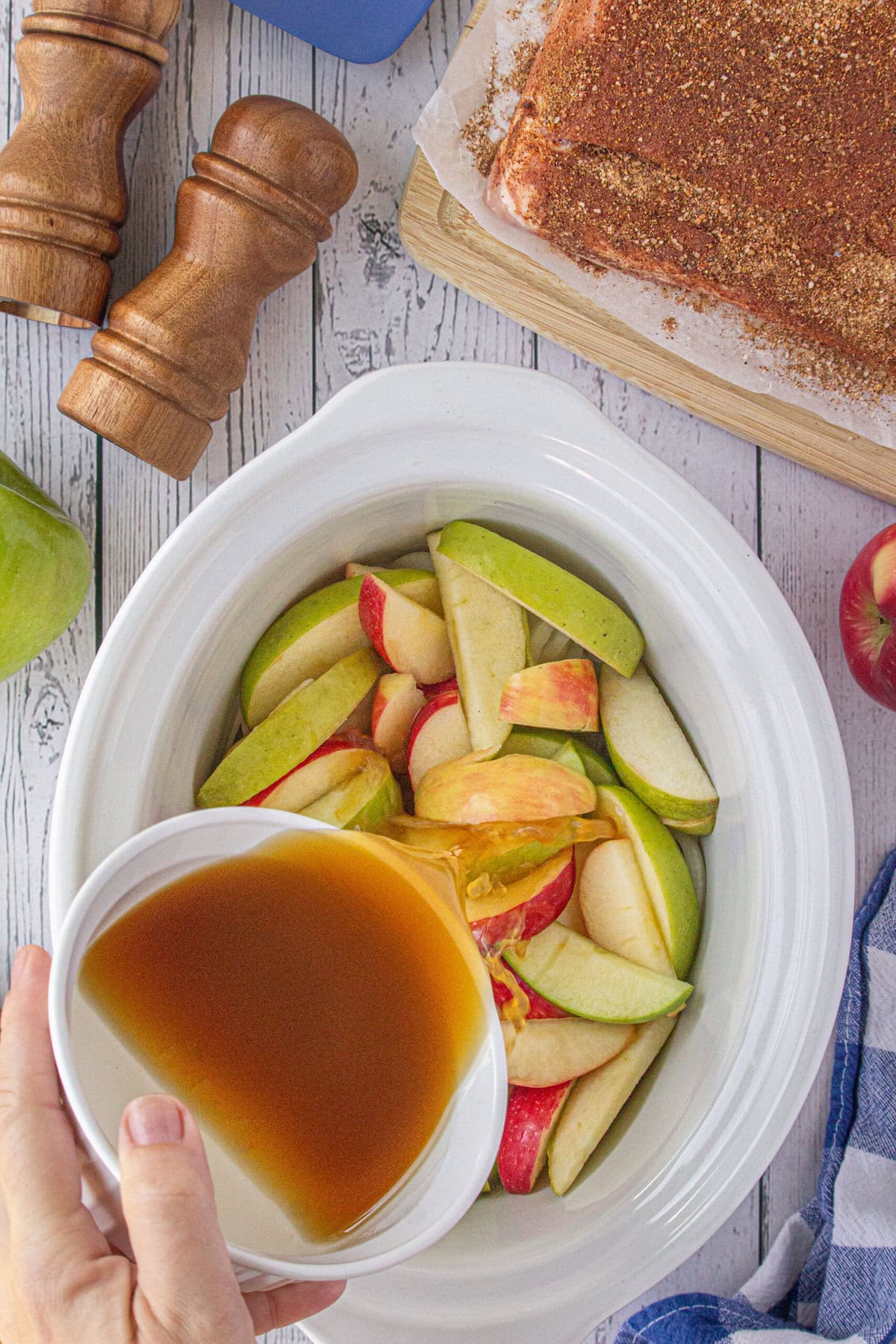 Pouring the brown sugar, lemon juice, and apple cider over the apples and onions in the slow cooker.