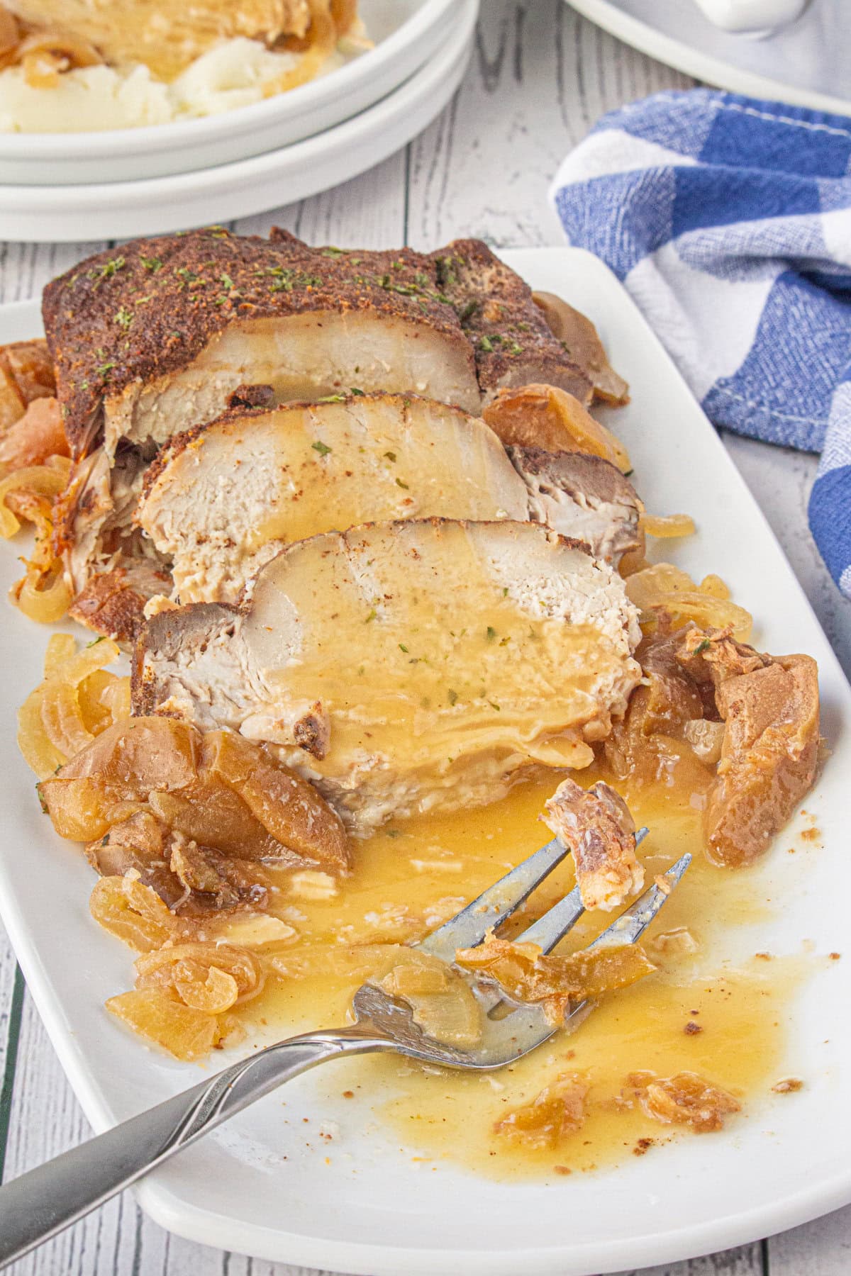 The pork roast sliced on a serving dish with apples, onions, and the apple cider sauce.