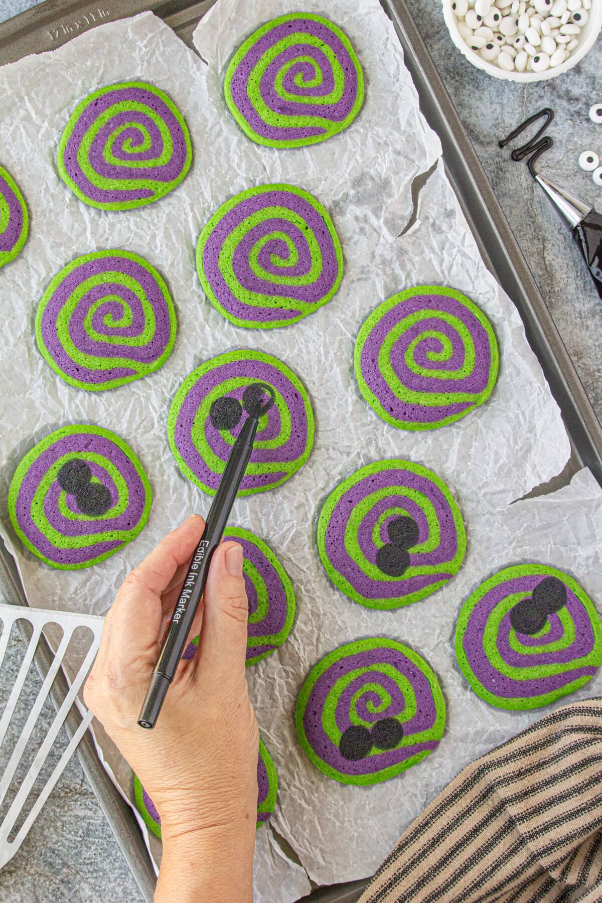 Black circles being painted on the cookies with edible marker.