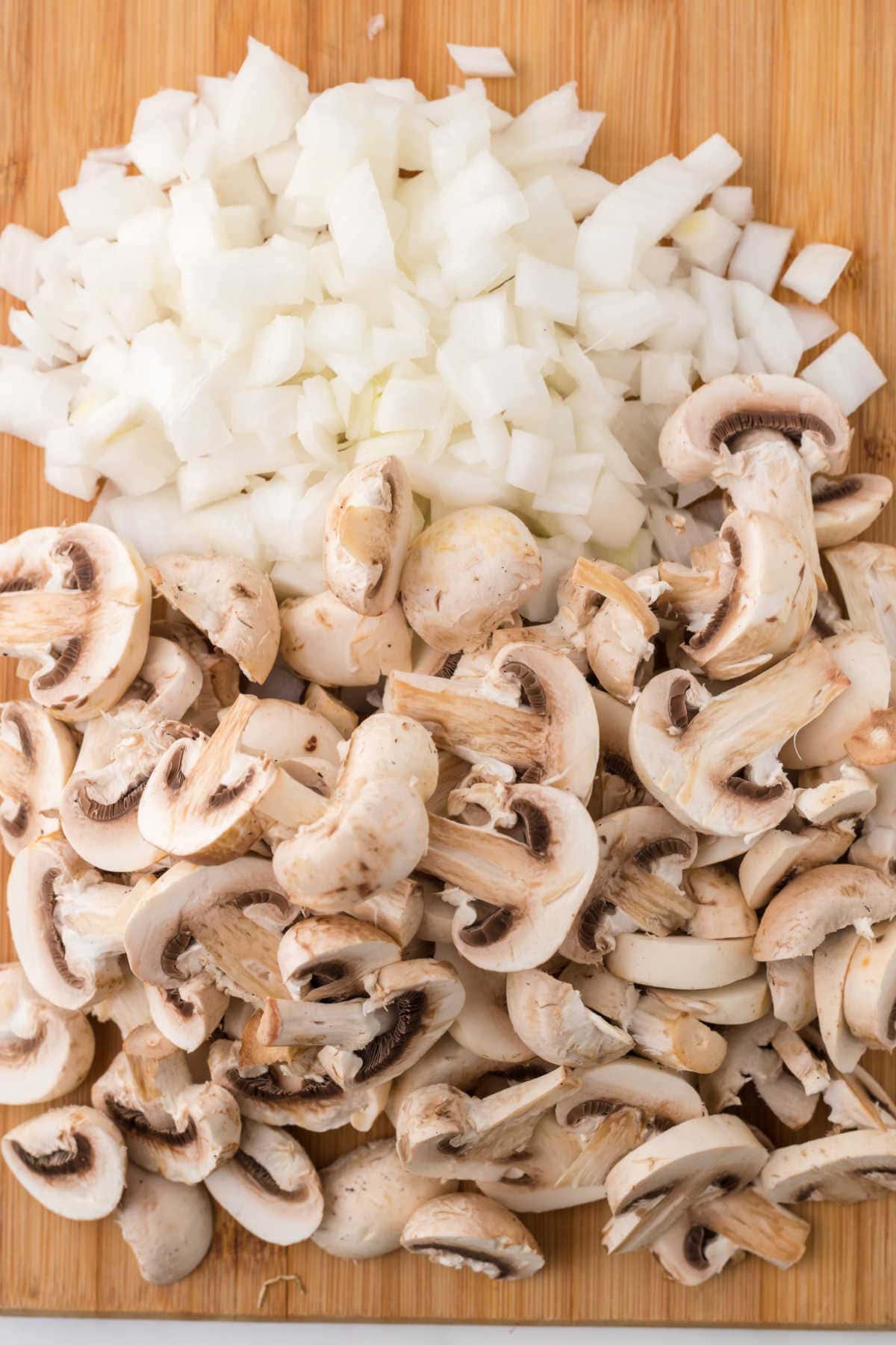 Sliced mushrooms and chopped onions on a cutting board.