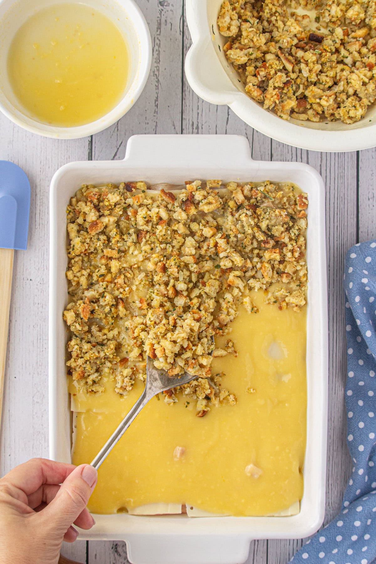 Spooning the prepared stuffing mix over the other ingredients in the casserole dish.