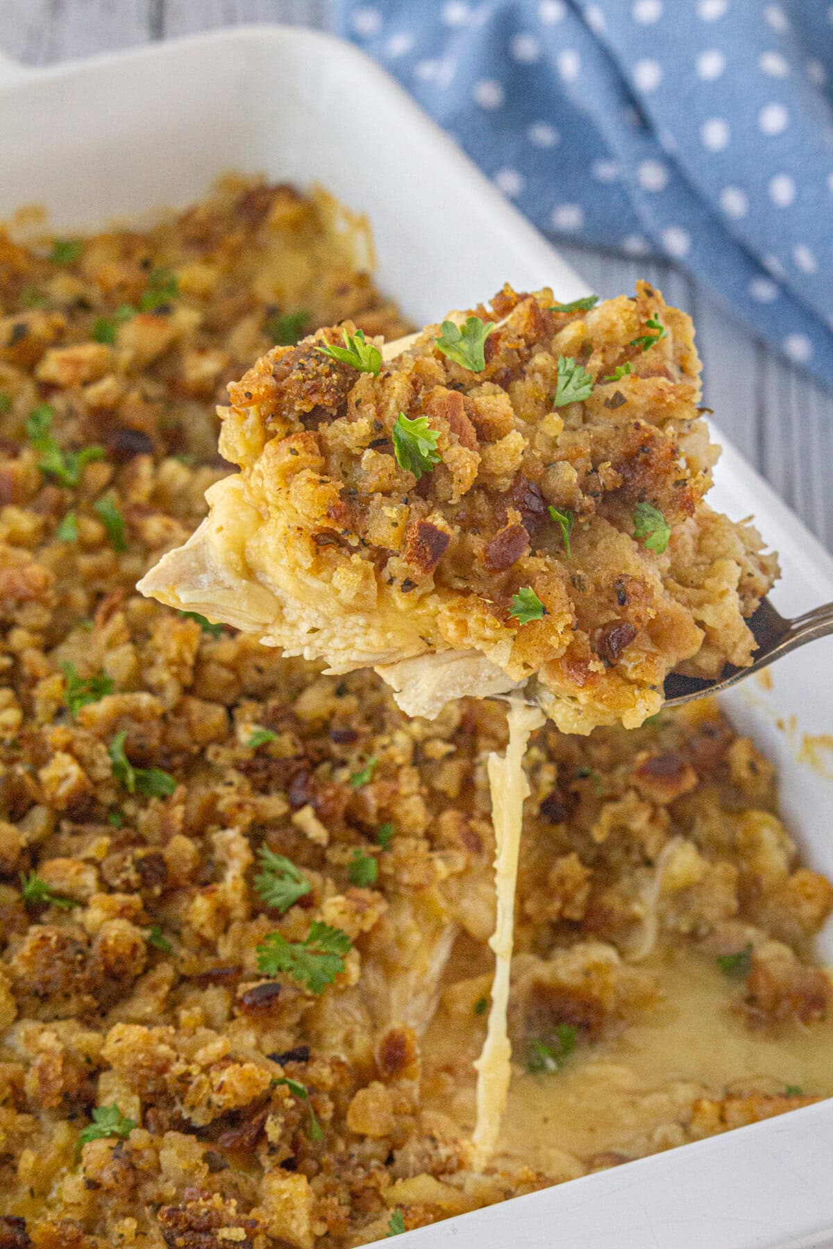 Scooping out a portion of chicken, stuffing, and Swiss cheese casserole from the baking dish.