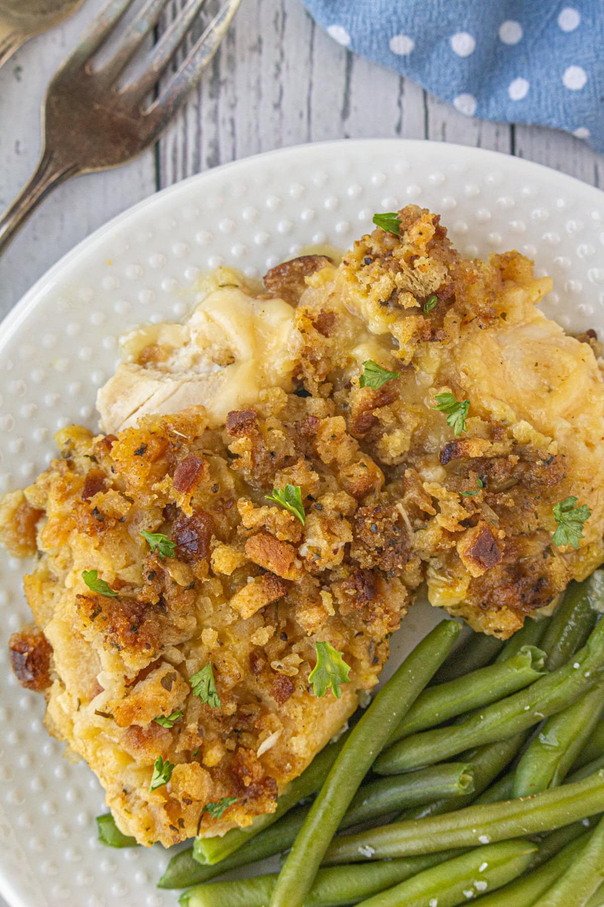 A portion of chicken, stuffing, and Swiss cheese casserole on a dinner plate next to green beans.