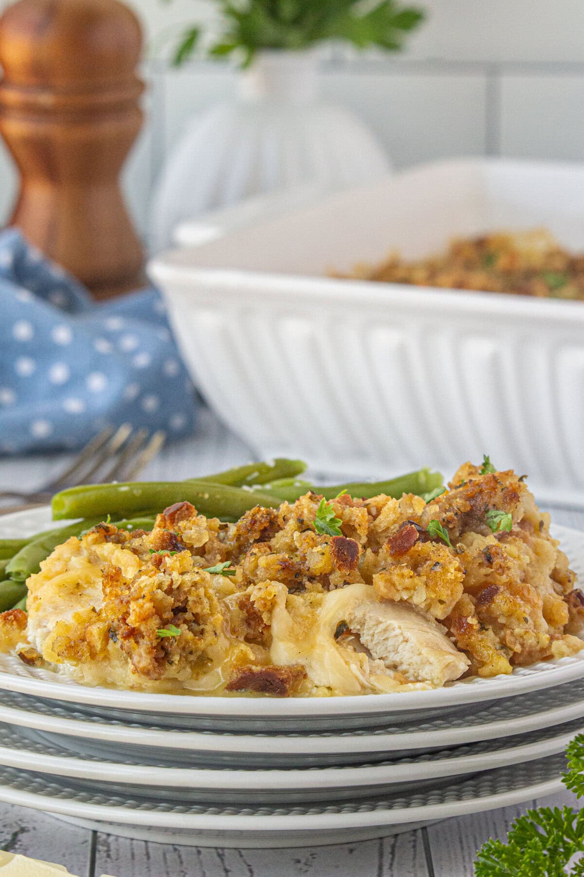 A side view of chicken, stuffing, and Swiss cheese casserole on a dinner plate with green beans.