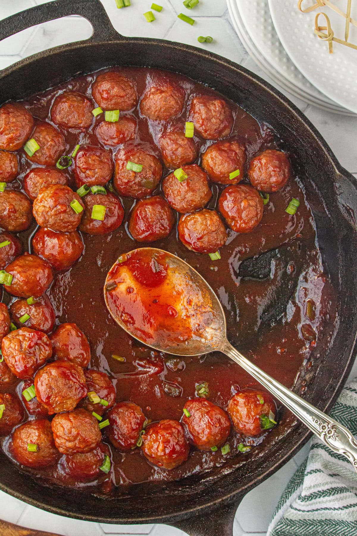 Cranberry sauce meatballs in a skillet with a serving spoon.