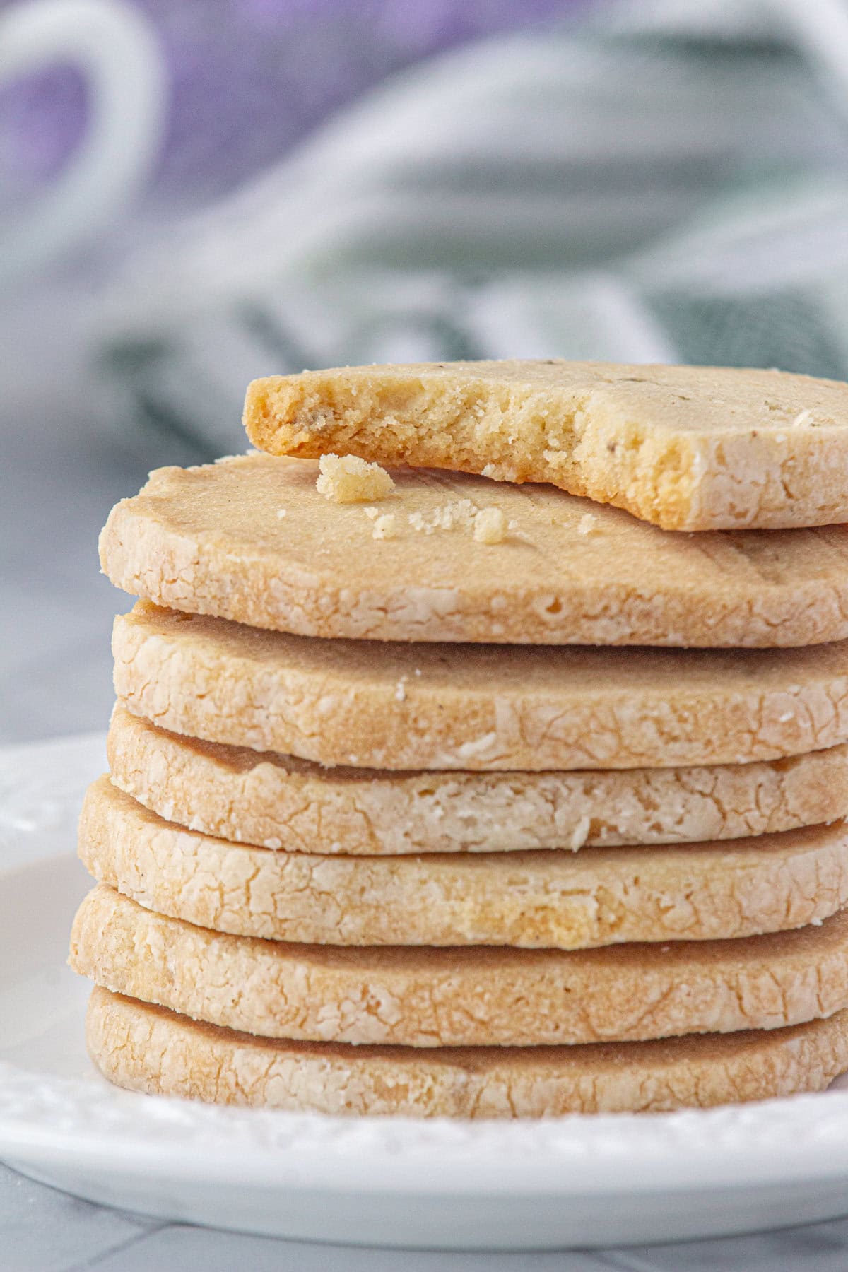 A stack of lavender shortbread cookies on a plate. The top cookie has a bite taken out.