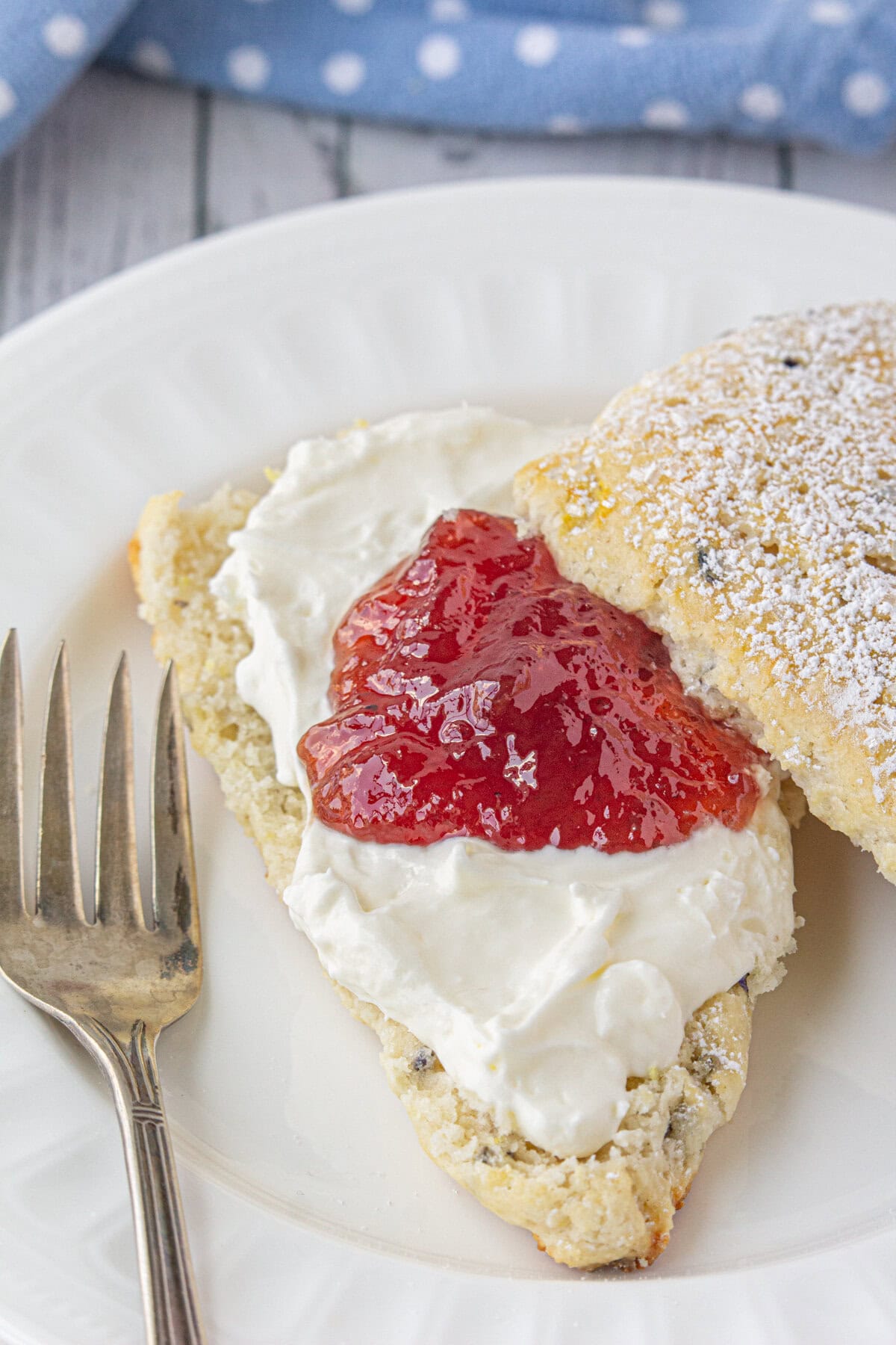 An up-close view of a scone sliced in half, topped with cream and jam.