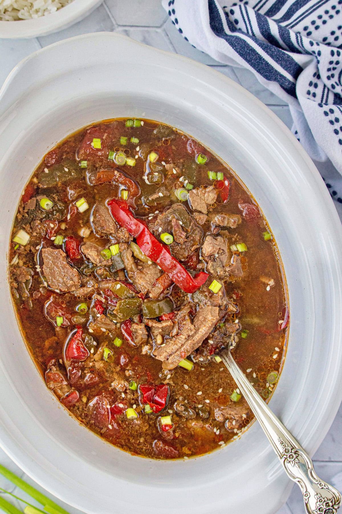 An overhead view of the pepper steak in the slow cooker with a serving spoon.