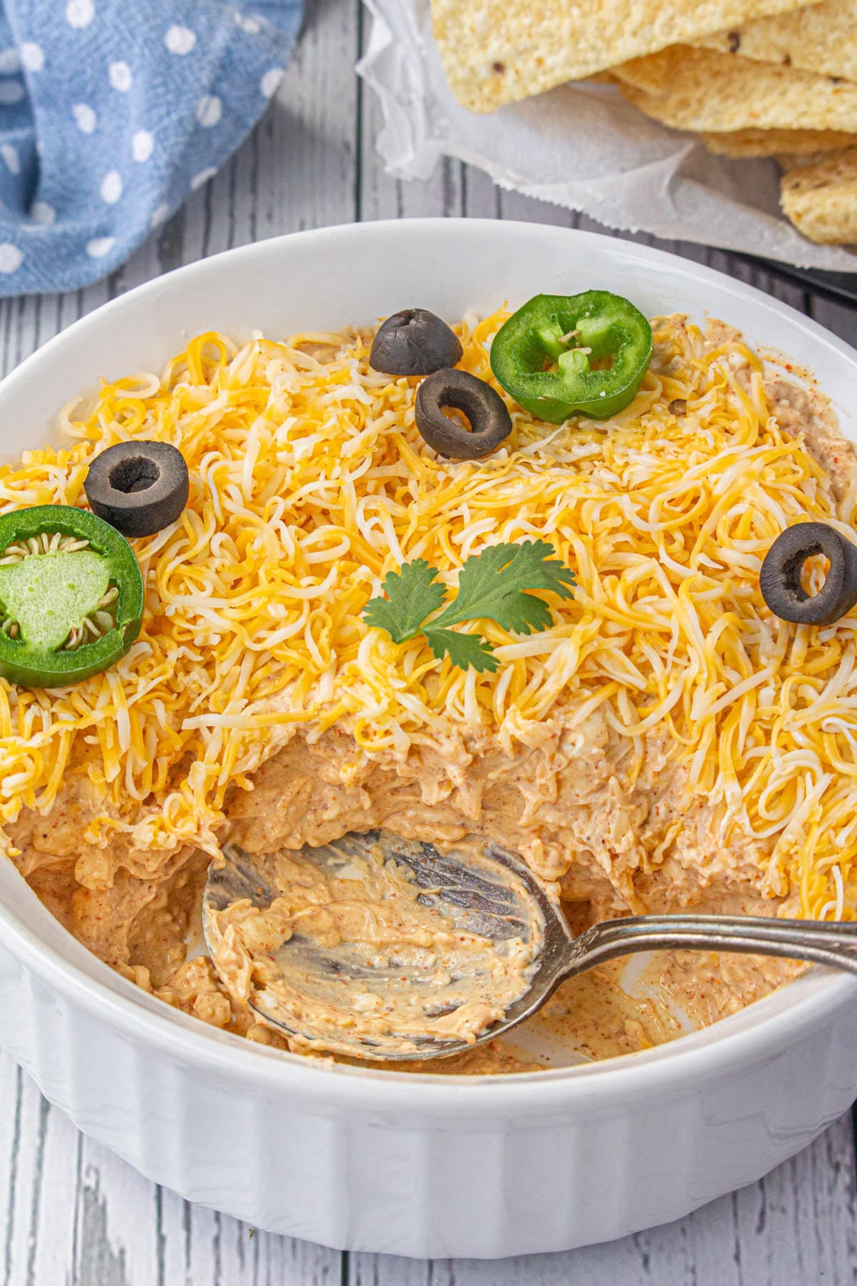 An angled view of the taco dip in a serving bowl with some of the dip eaten already.