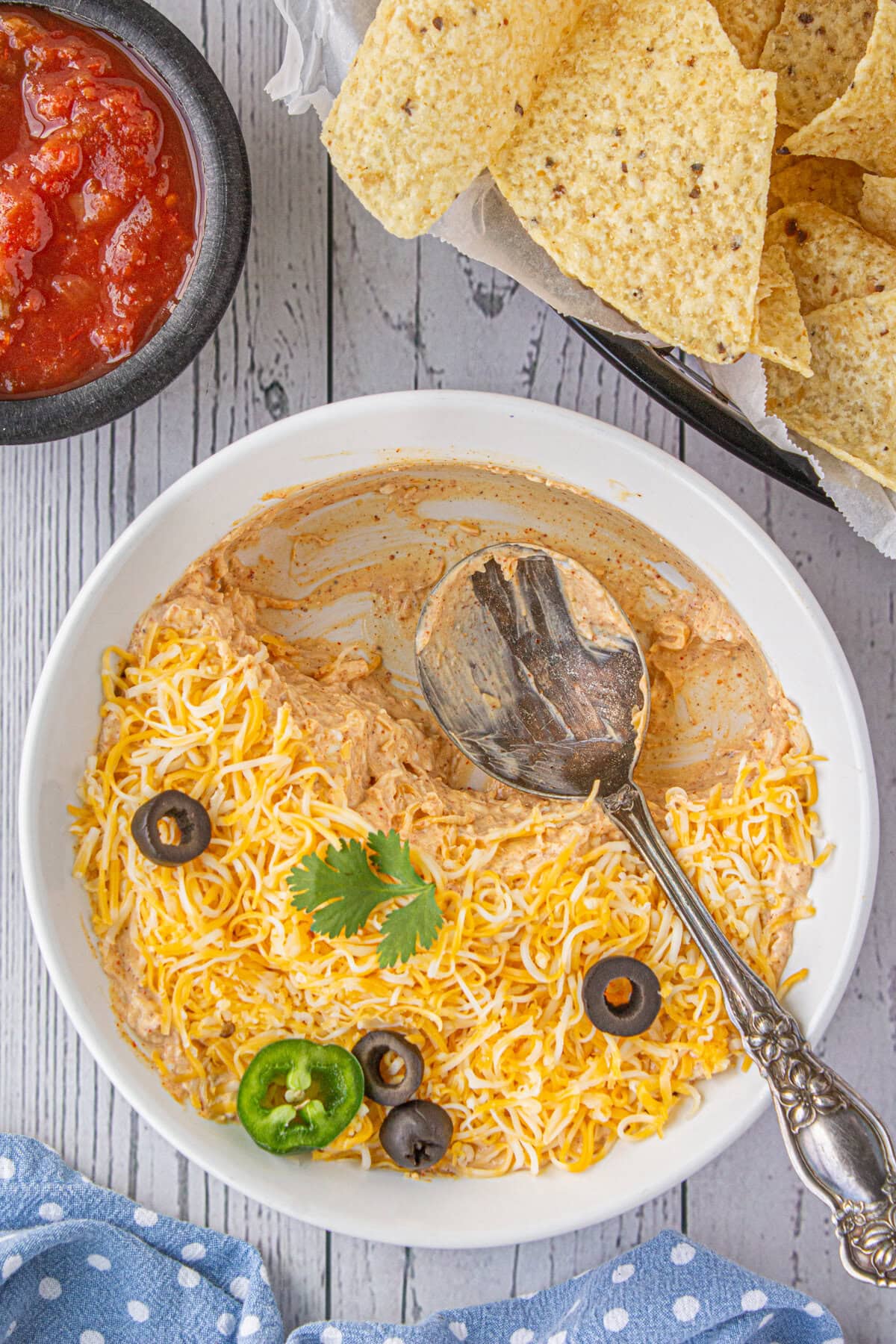 Four ingredient taco dip in a serving bowl with a spoon and some dip already eaten.