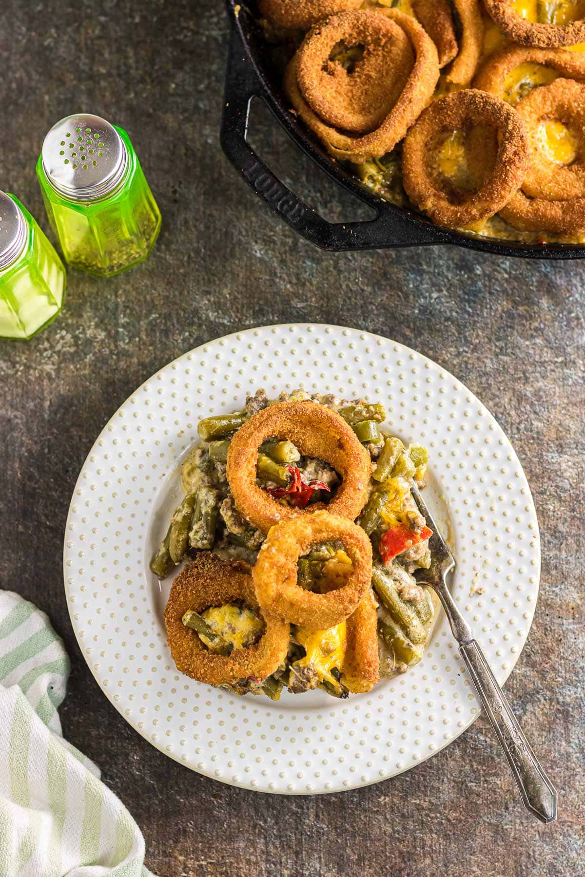 An overhead view of green bean and ground beef casserole with onion rings on a dinner plate.