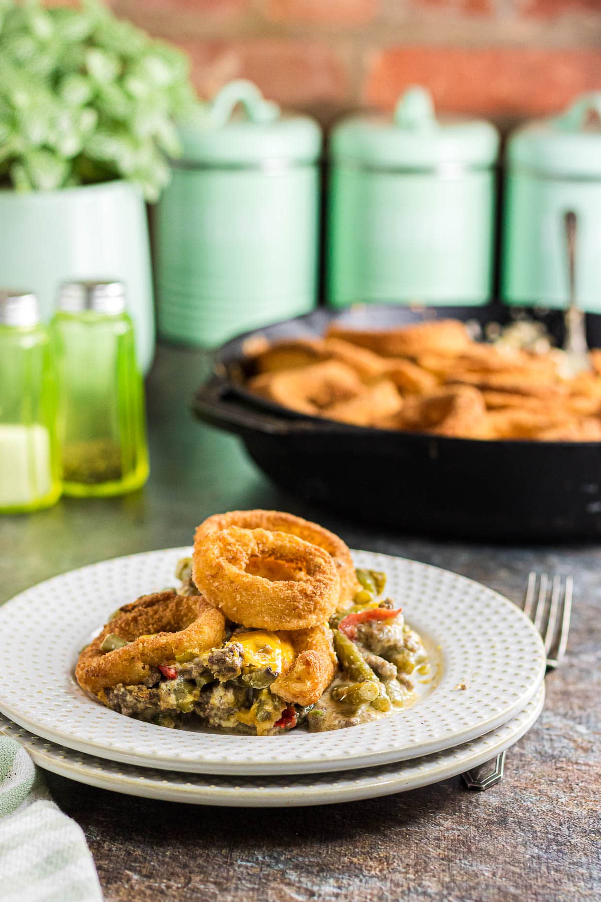 A side view of green bean and ground beef casserole topped with onion rings on a dinner plate.