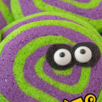 Closeup of green and purple pinwheel cookies with candy eyes. Title text overlay for Pinterest.