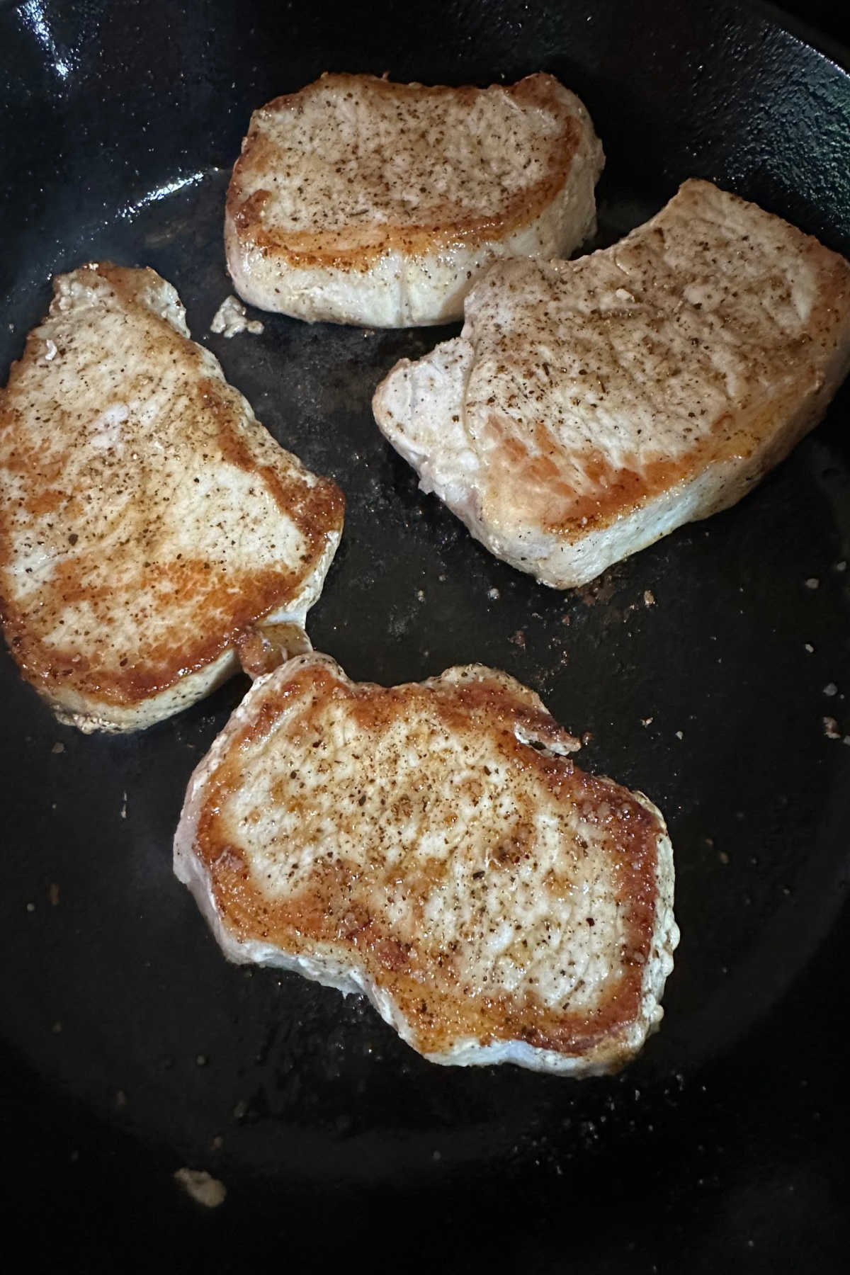 Pork chops searing in a hot skillet.