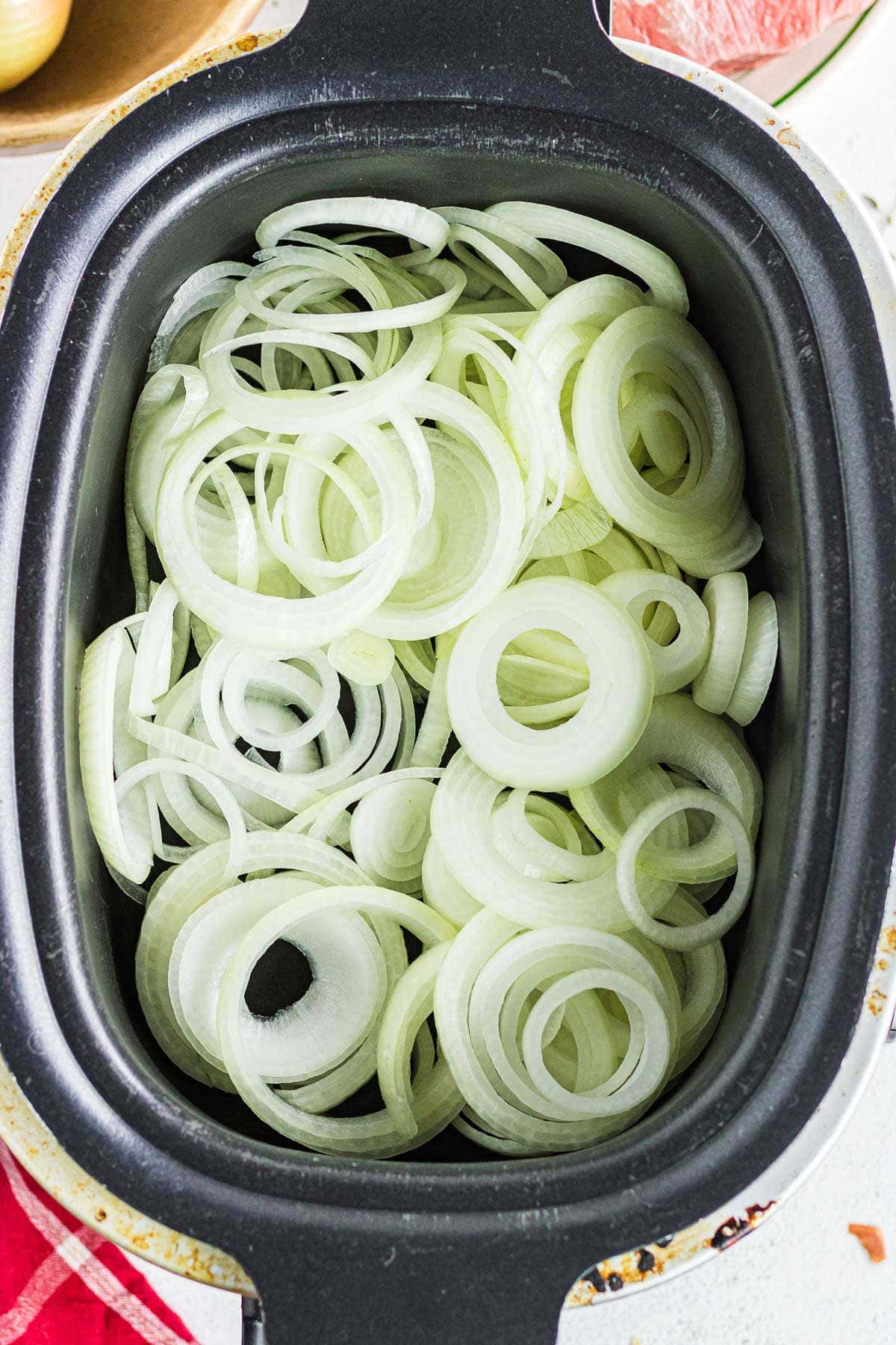 Sliced onions layered in the bottom of the slow cooker.