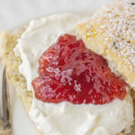 A lavender scone with clotted cream and strawberry jam on a plate. Title text overlay for Pinterest.