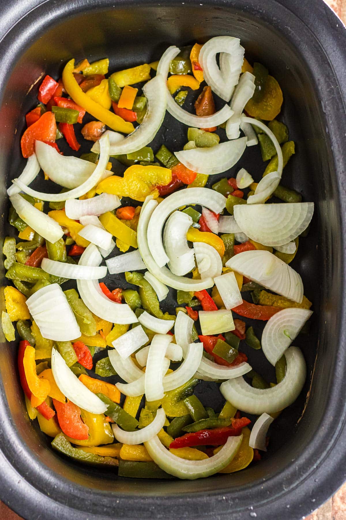 The frozen bell peppers and sliced onions in the slow cooker.