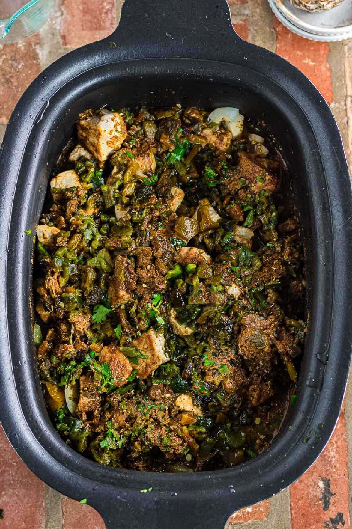 The chopped peppers, seasoning, cilantro, and broth added to the slow cooker.