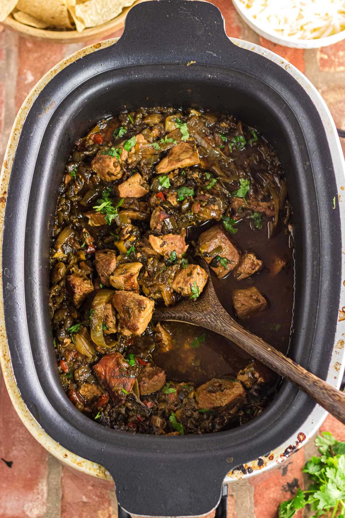 Overhead view of pork chile verde in the slow cooker with a wooden serving spoon.