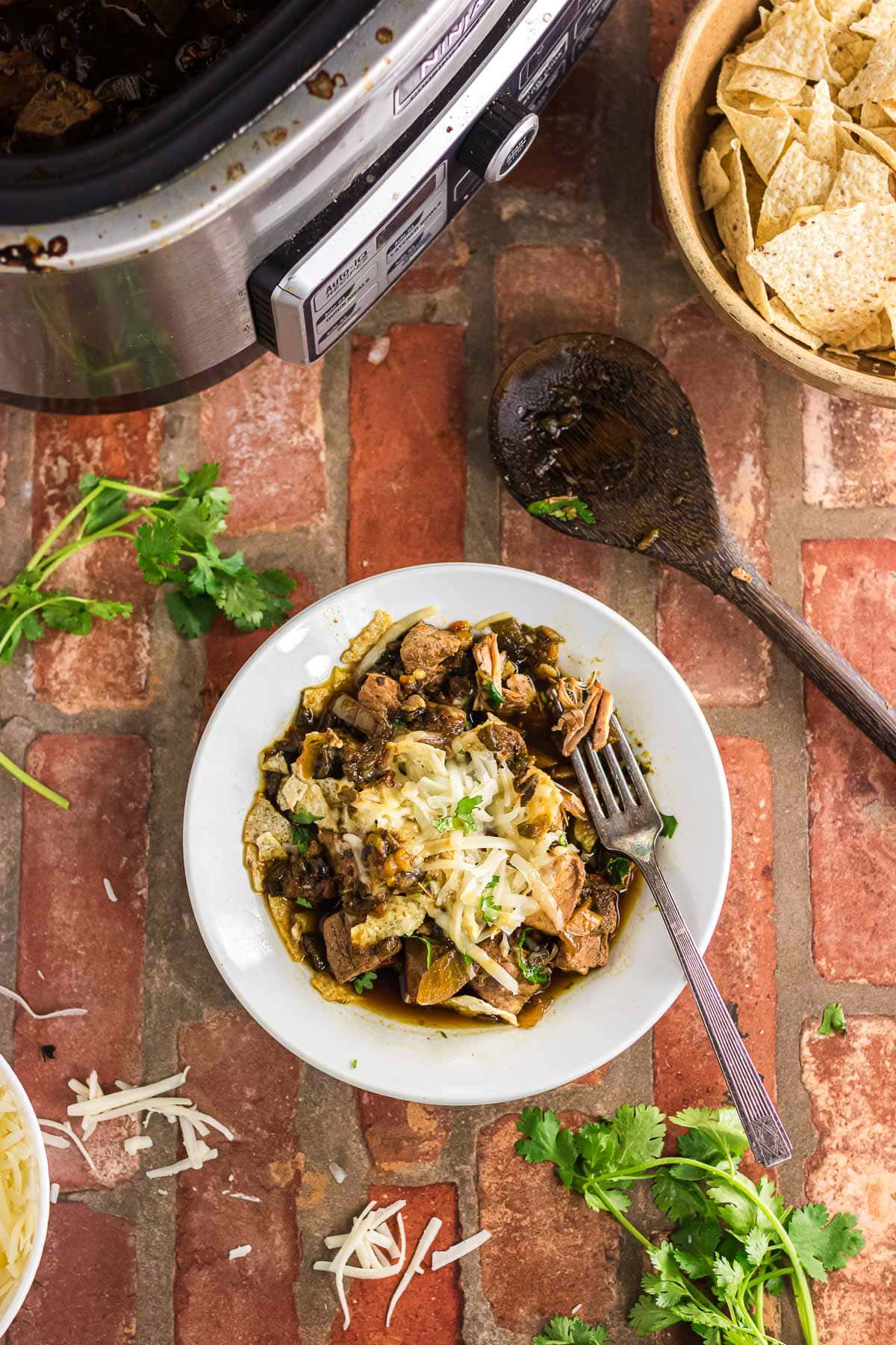 A dinner bowl with pork chile verde topped with cheese and more cilantro.