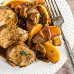 Pork tenderloin sliced on a white plate surrounded by cooked apples.