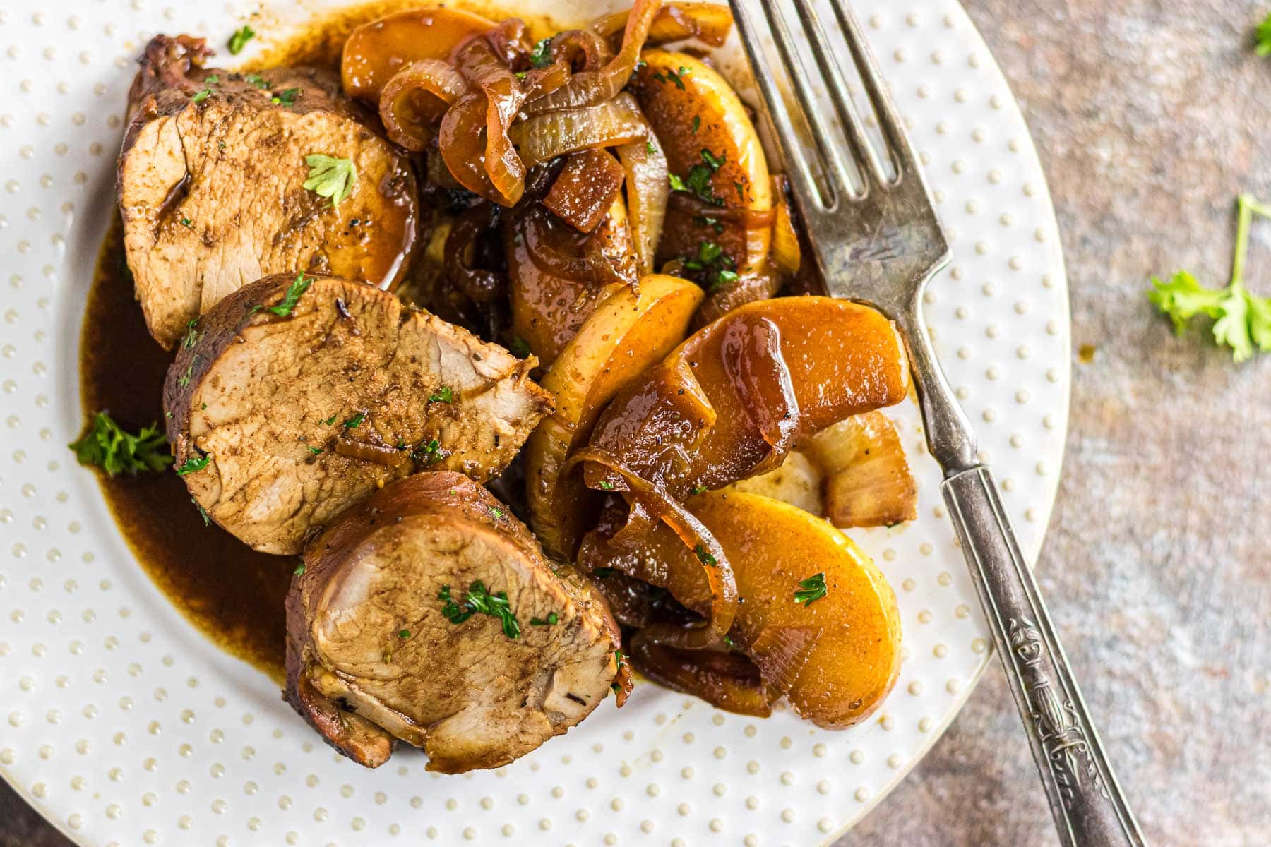 Pork tenderloin sliced on a white plate surrounded by cooked apples.