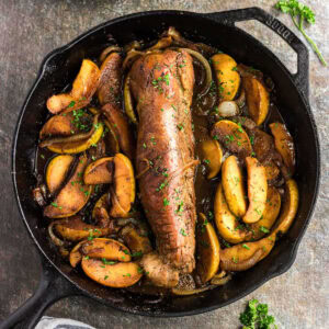 Overhead view of pork tenderloin in cast iron skillet surrounded by apples.