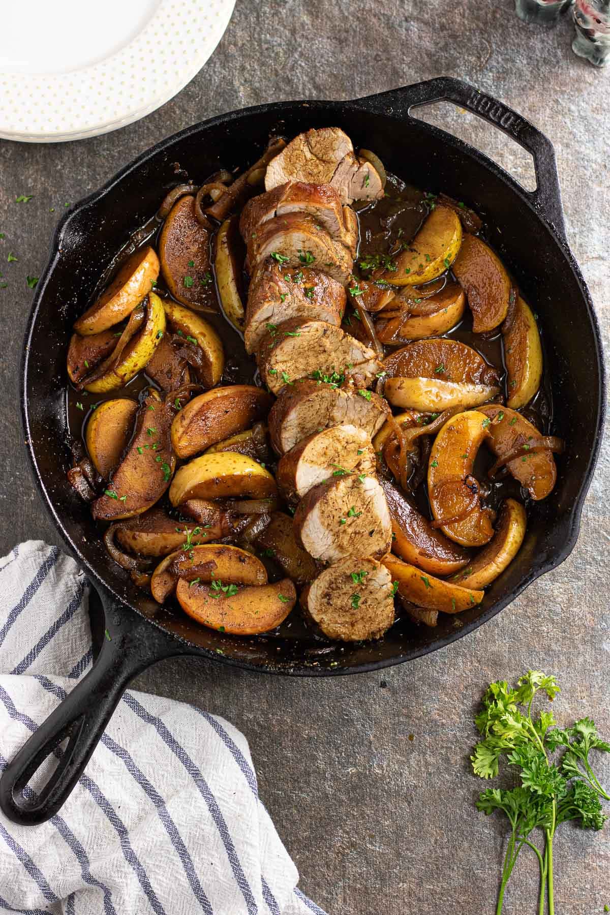 The sliced pork tenderloin in the skillet with the onions and apples.