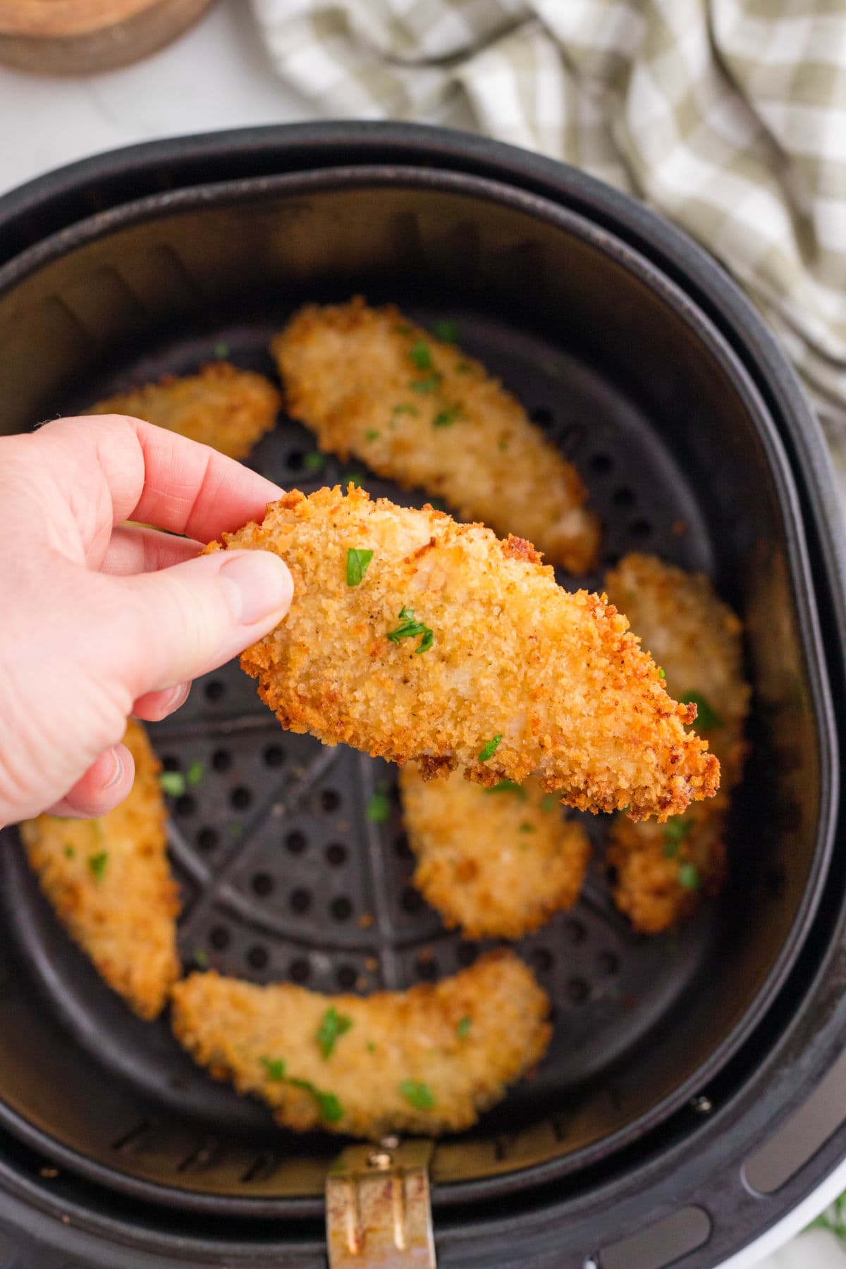 Fingers picking up crispy chicken tenders from the air fryer.