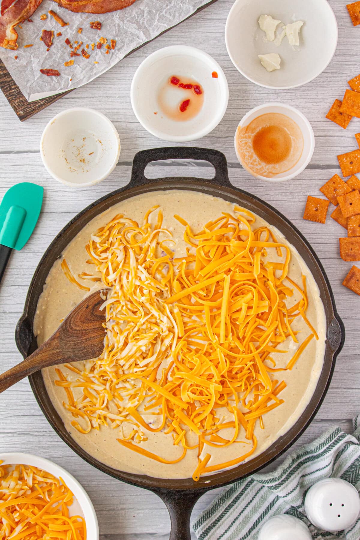 Stirring the pimentos, bacon, and shredded cheese into the milk mixture to make cheese sauce.