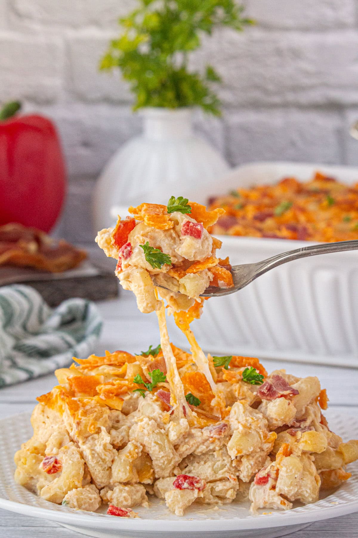 A fork scooping up a bite of bacon pimento mac and cheese from a dinner plate.