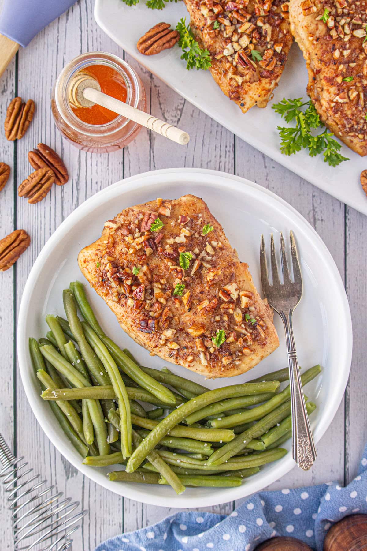 An overhead photo of a honey pecan chicken breast on a dinner plate with green beans.