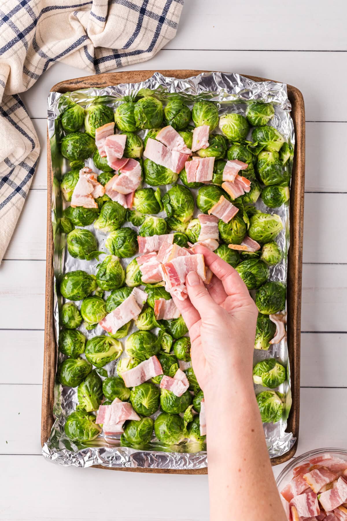 Uncooked bacon is added to the top of the Brussels sprouts.