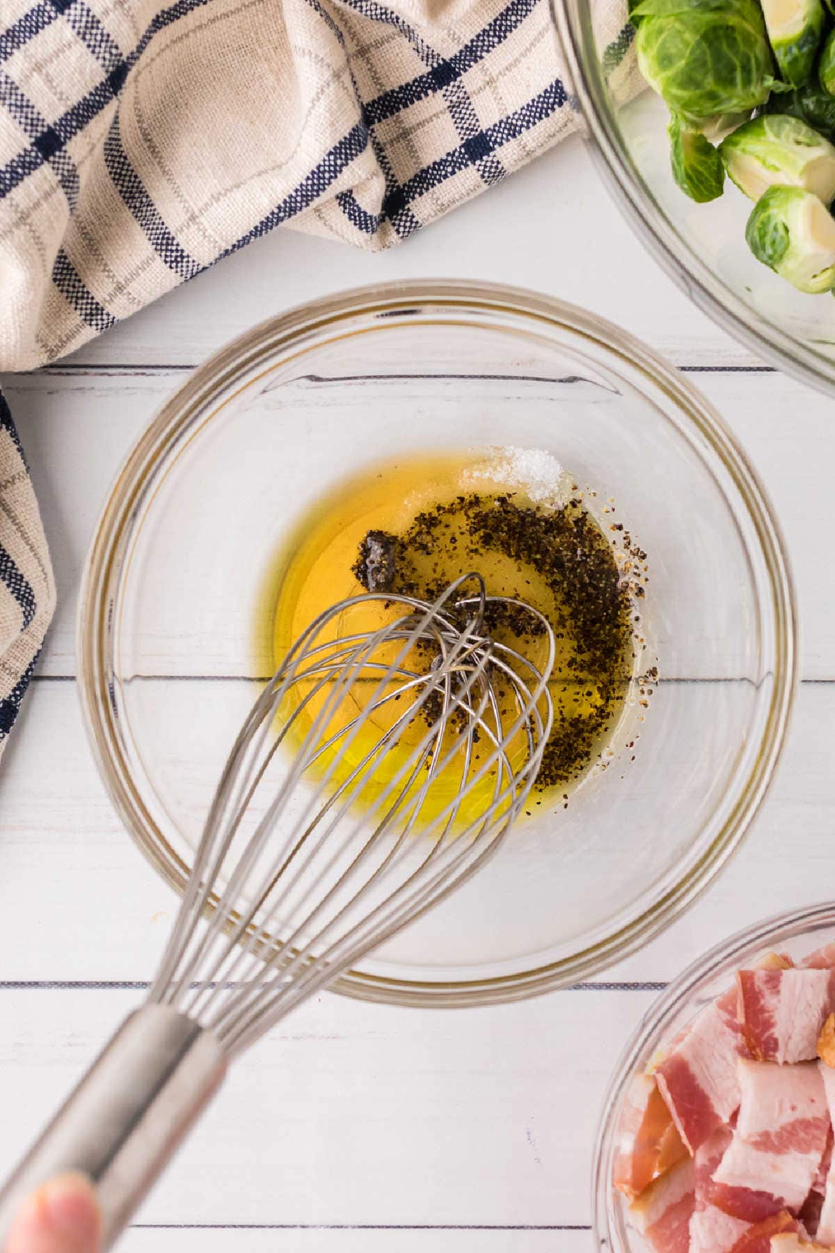 Olive oil, maple syrup, and seasoning being whisked in a bowl.