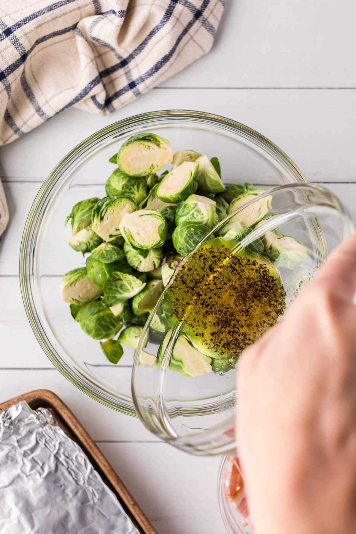 The olive oil mixture is poured over the cut Brussels sprouts.