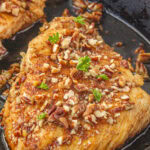 Closeup of a chicken breast with pecans on it in a iron skillet with a title text overlay for Pinterest.