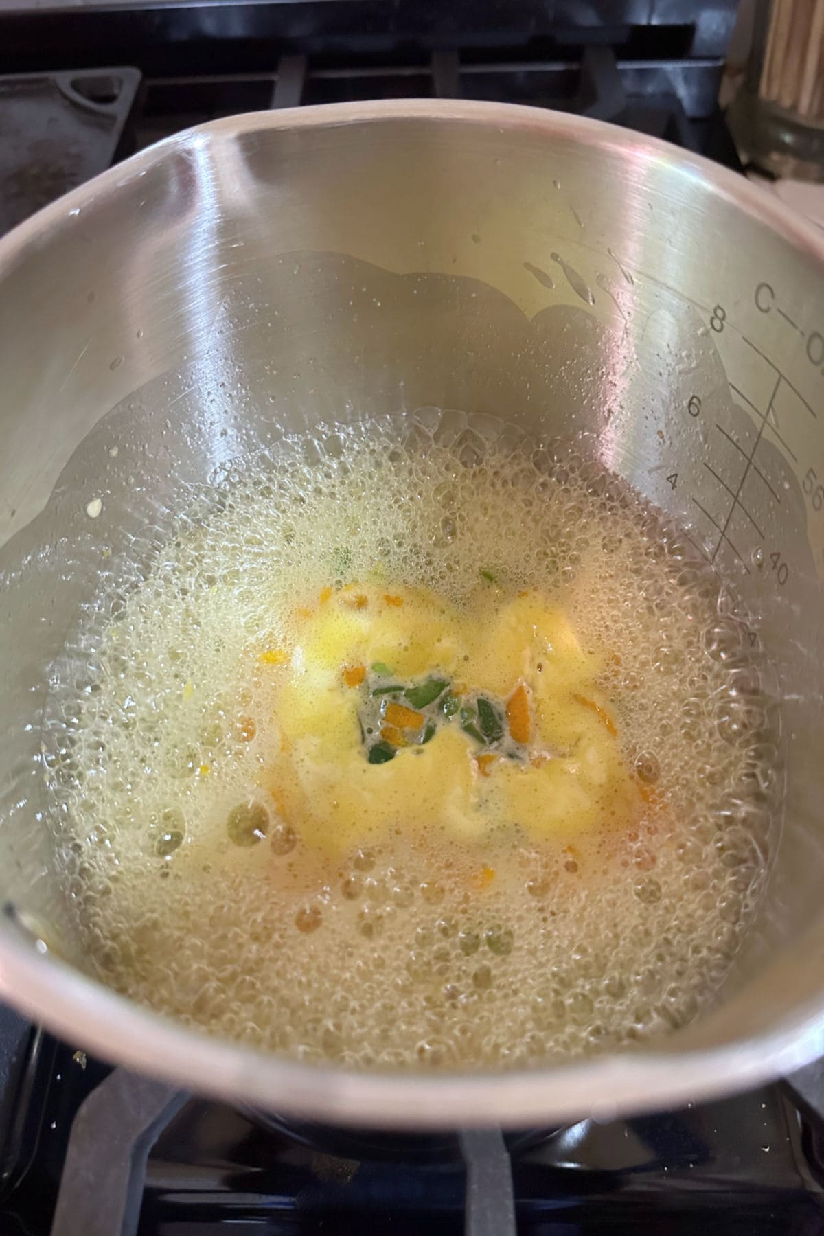 Simmering the jalapenos, sugar, orange juice, and orange zest in a saucepan.