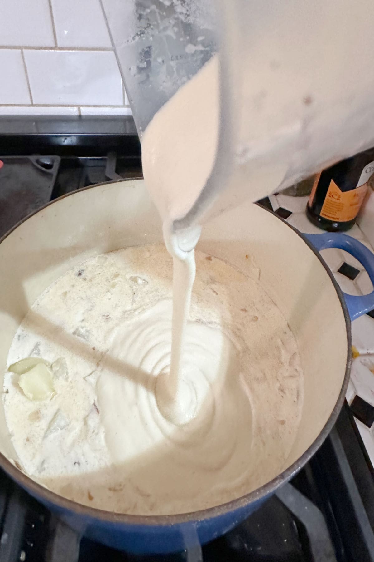 Pouring the blended cup of soup into the potato soup mixture in the Dutch oven.