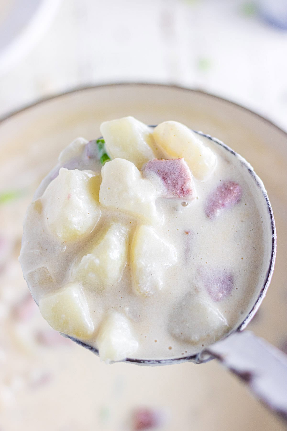 A close-up photo of smoked sausage potato soup in a ladle.