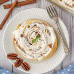 Large cinnamon roll with gooey icing on a white plate.